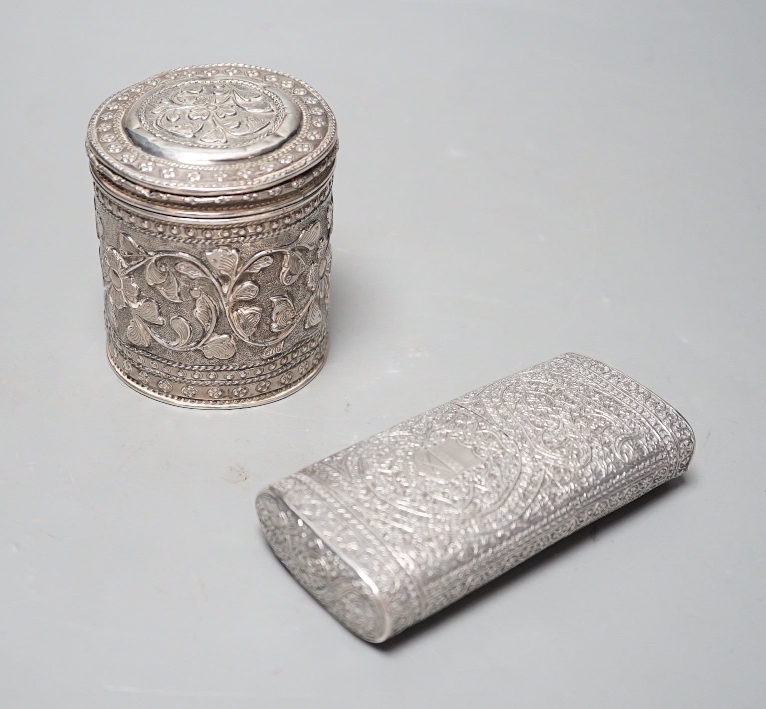An Indian embossed white metal cigar case, 12.2cm and a similar canister and cover.